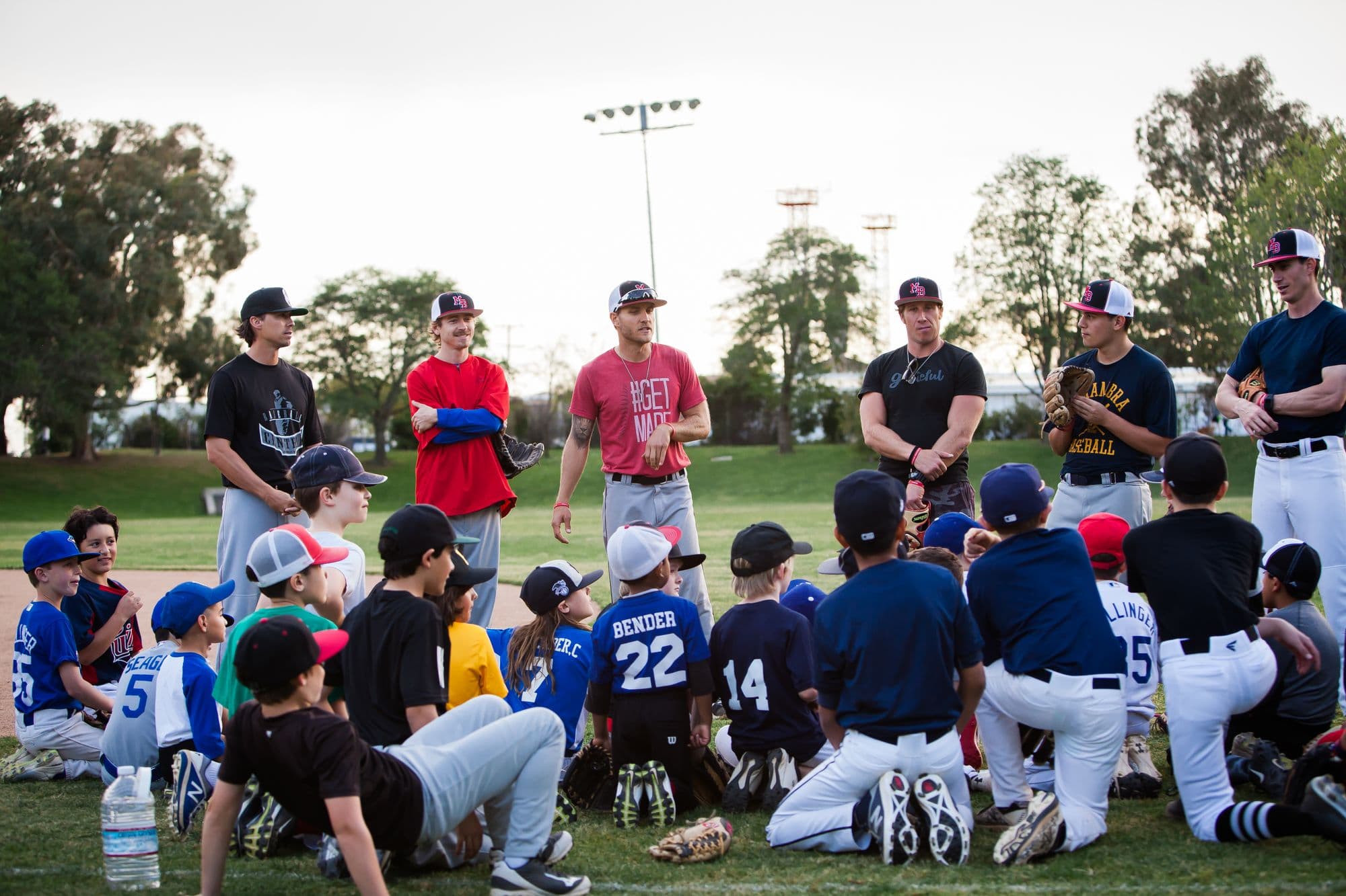 Six MADE Baseball coaches standing in front of a large group of seated campers at the start of a session