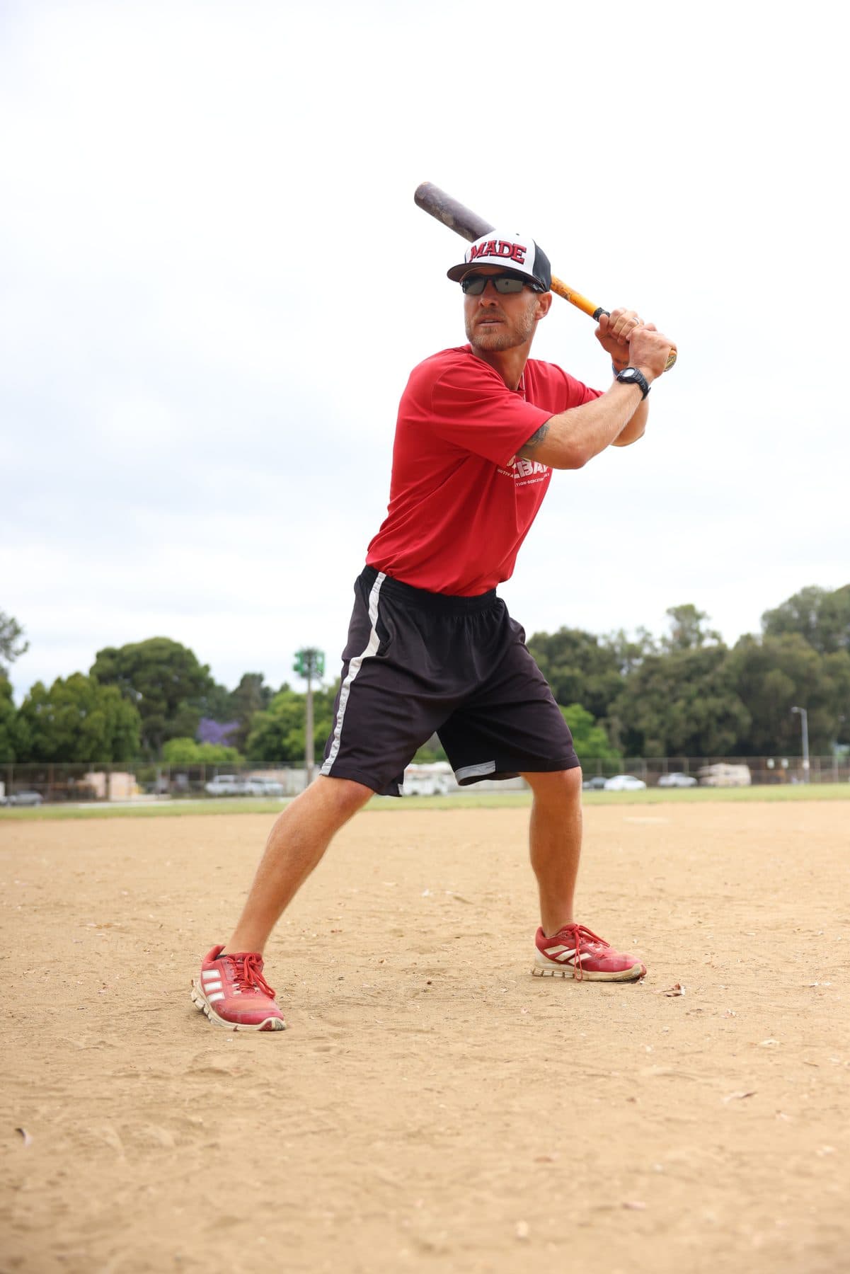 Coach Isaac Hess in a MADE cap demonstrating a batting stance with a bat on his shoulder