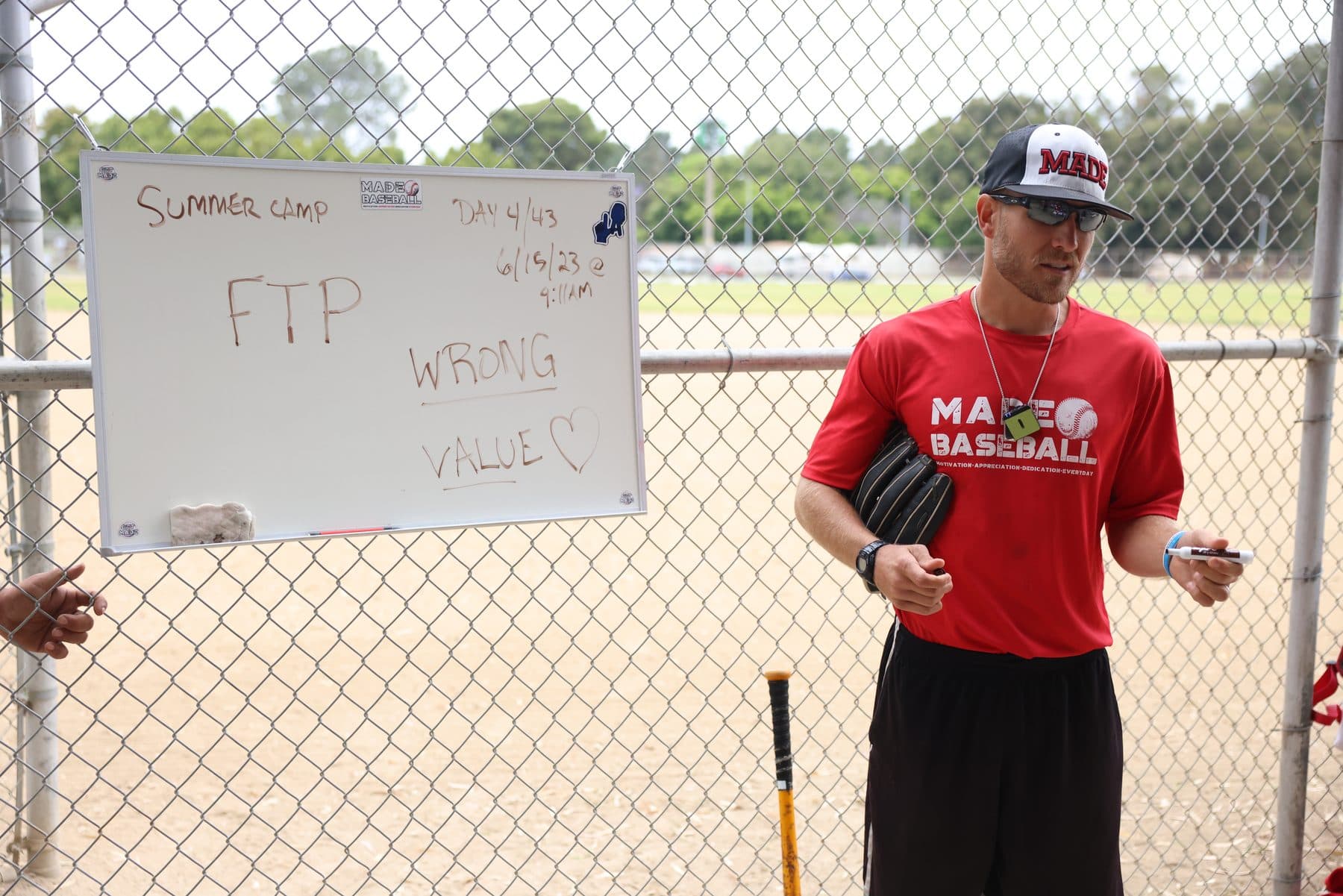 Coach Isaac Hess in a red MADE shirt explaining a point beside a whiteboard
