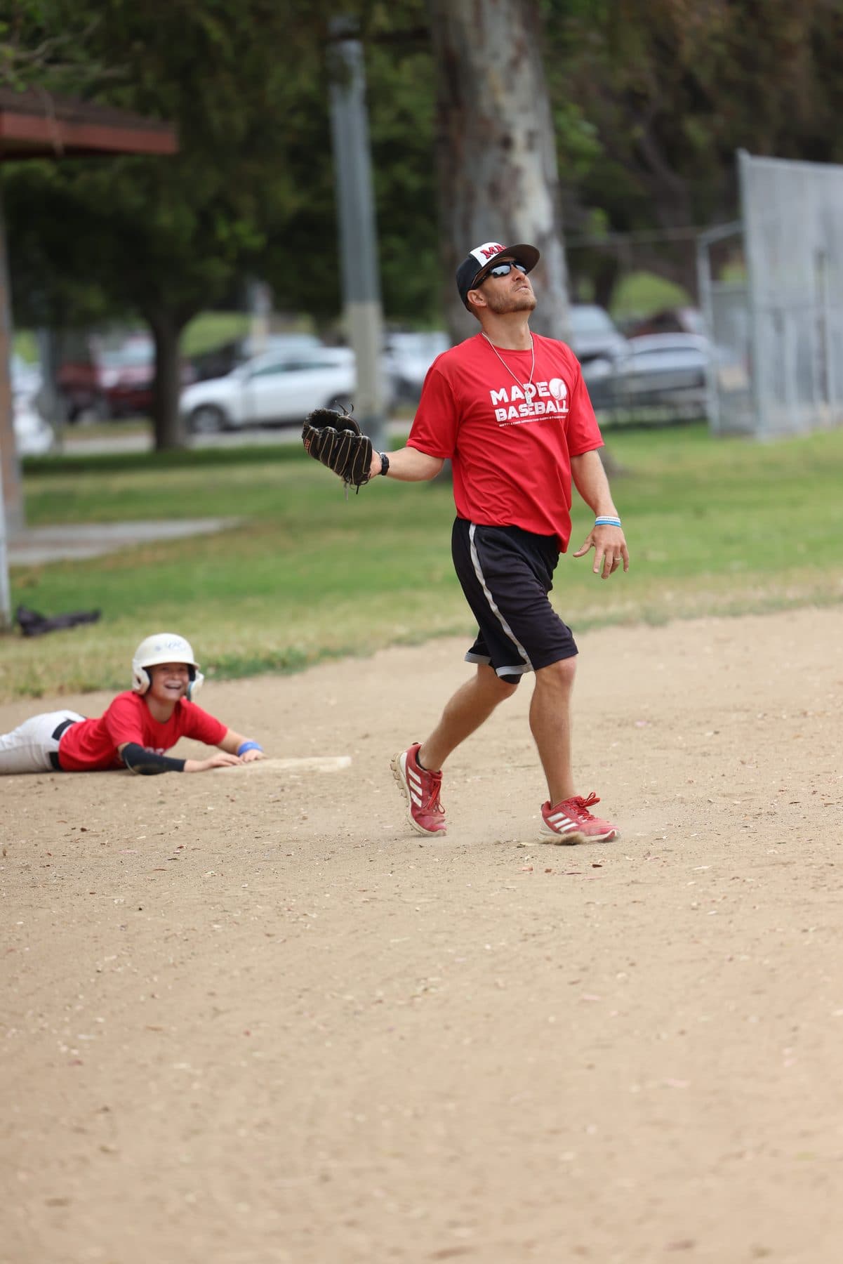 Coach Isaac Hess reacting during a fly-ball drill while a player lies on the ground behind him