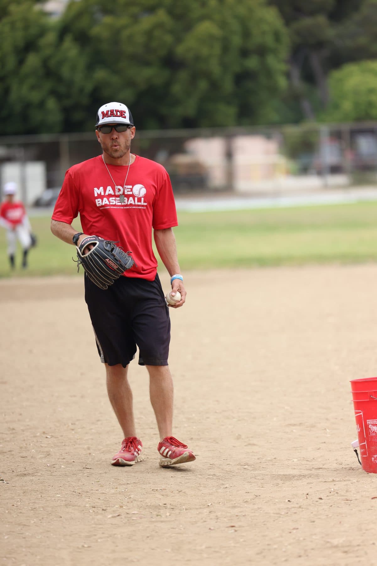 Coach Isaac Hess in a red MADE shirt standing on the infield with his glove in hand