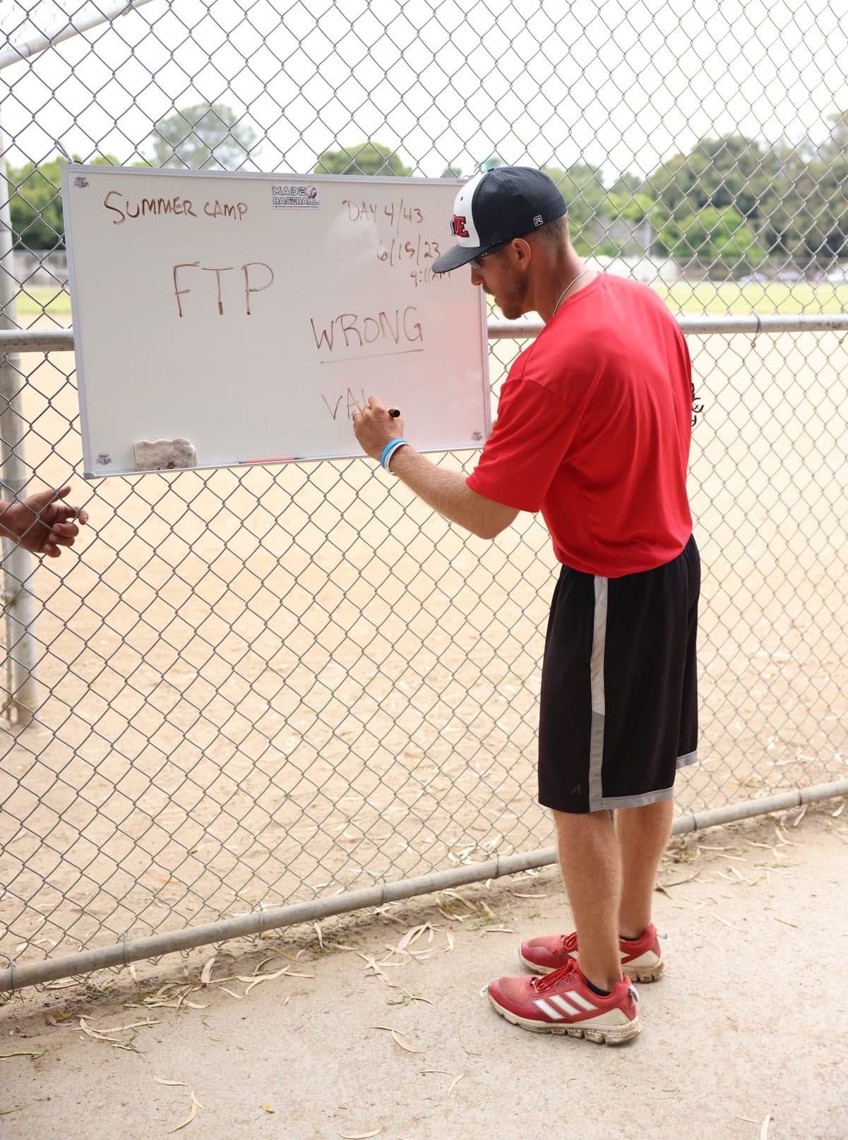 Coach Isaac Hess writing on a whiteboard hung on a chain-link fence during a camp session