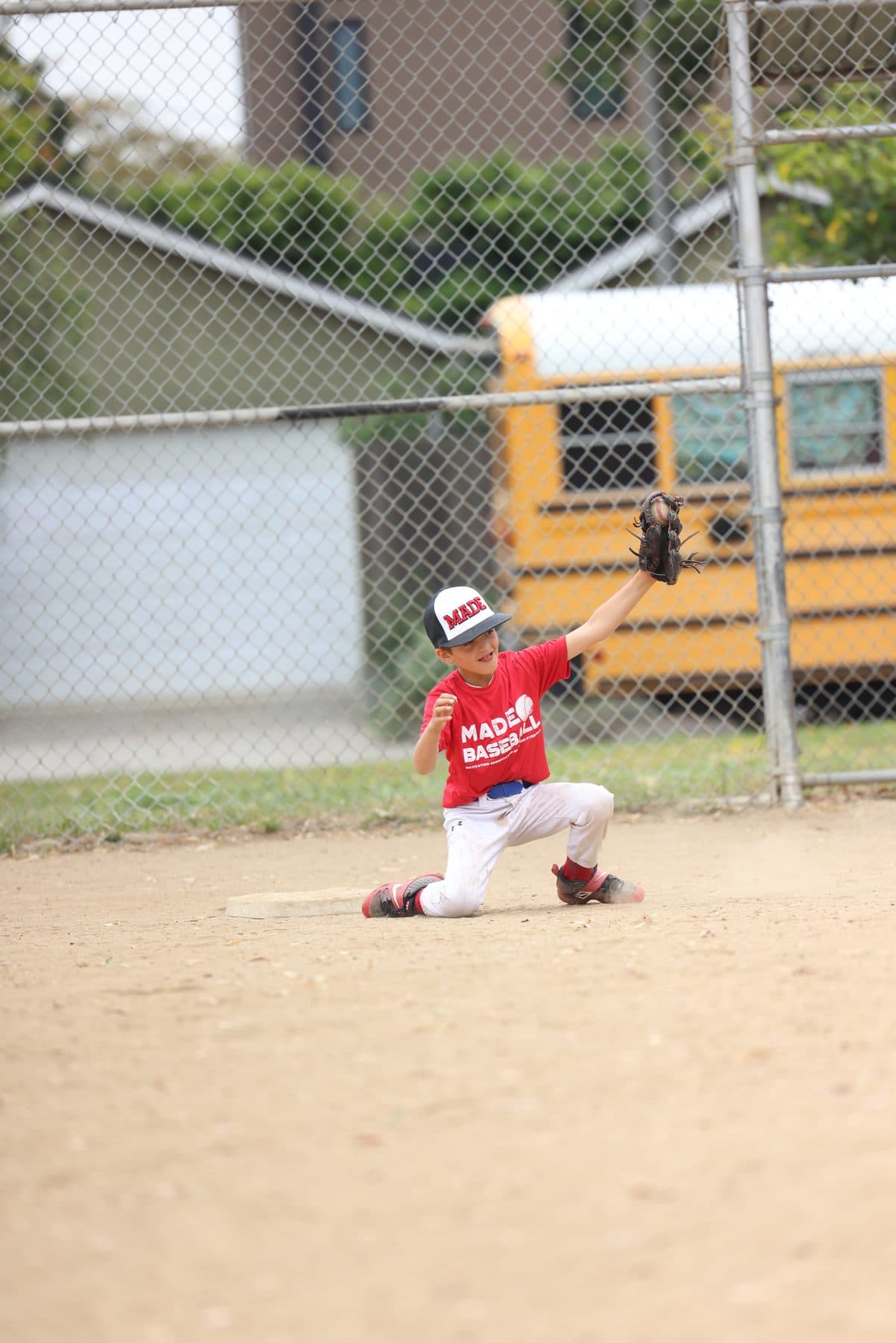 A young player in a red MADE shirt kneeling with his glove up, ready to catch