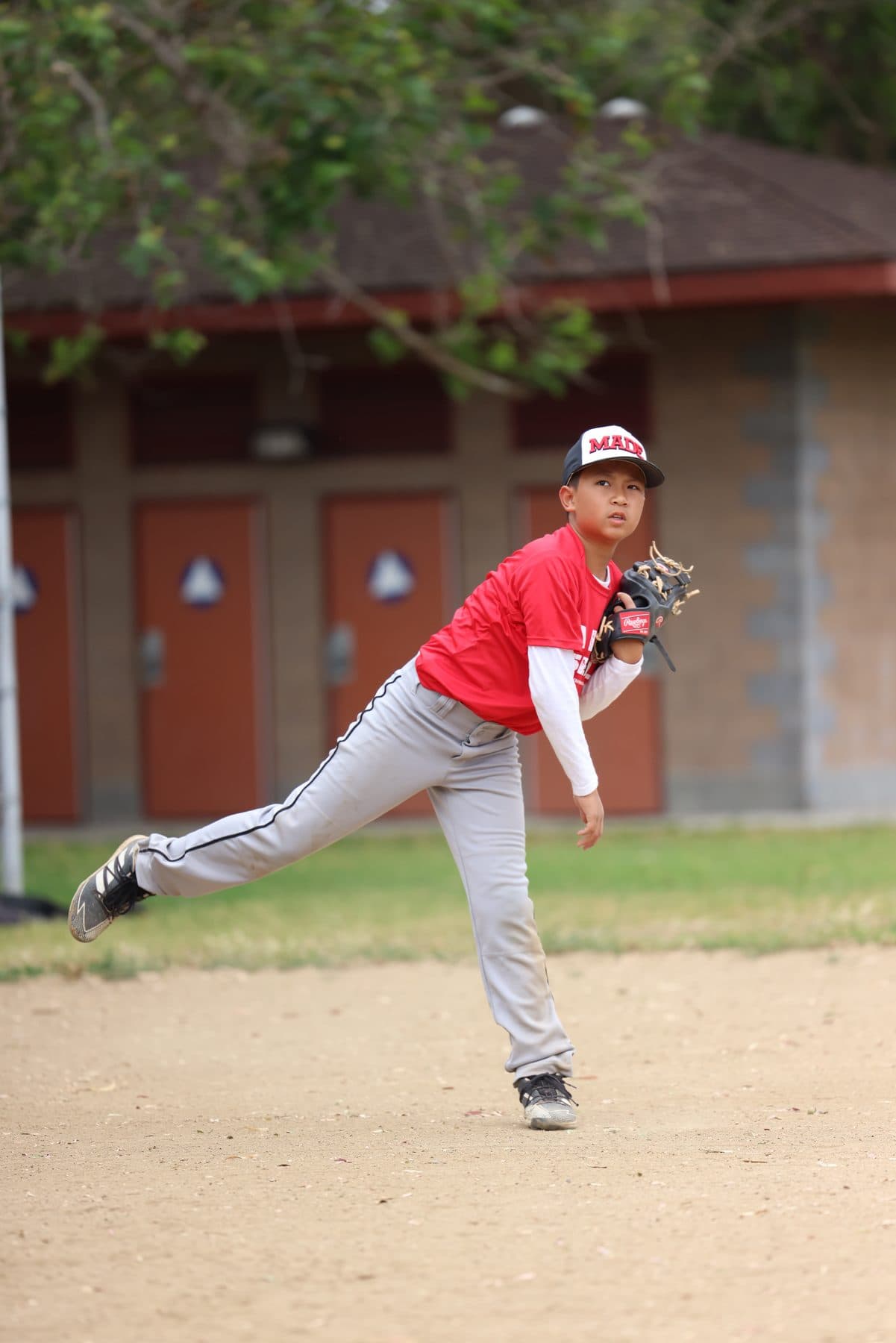 A young pitcher in a red MADE shirt following through after a throw on a dirt mound