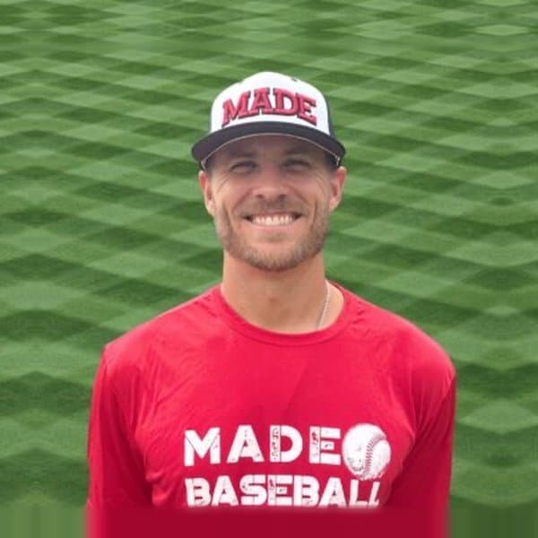 Coach Isaac Hess smiling in a MADE Baseball cap and red MADE Baseball shirt