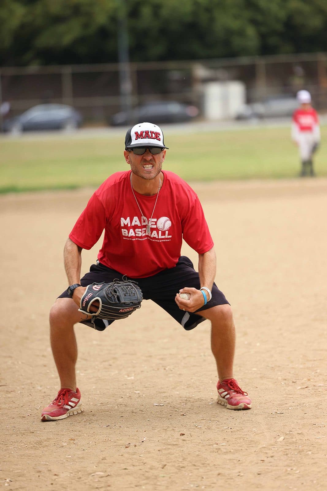 Coach Isaac Hess in a red MADE Baseball shirt, crouched in a ready fielding stance with a glove