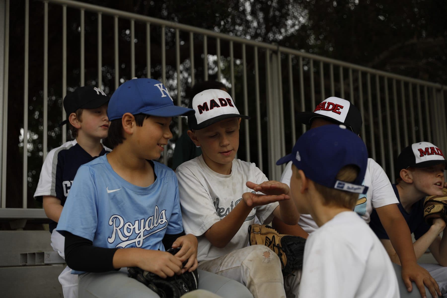Young players in MADE caps and team jerseys grin and joke with each other on the bench between drills