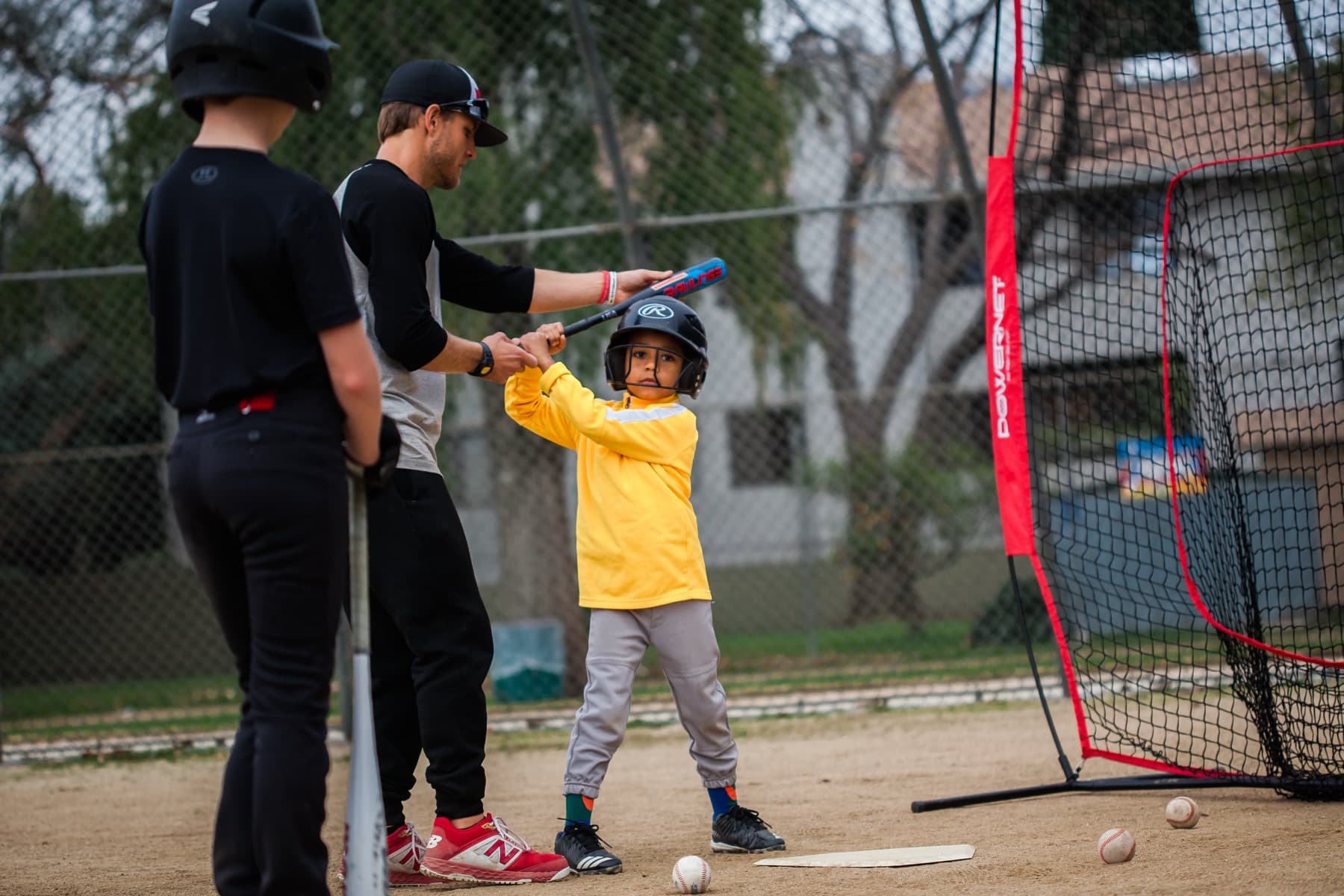 Coach Isaac Hess steadying a young hitter's bat and stance at the batting net during a private lesson