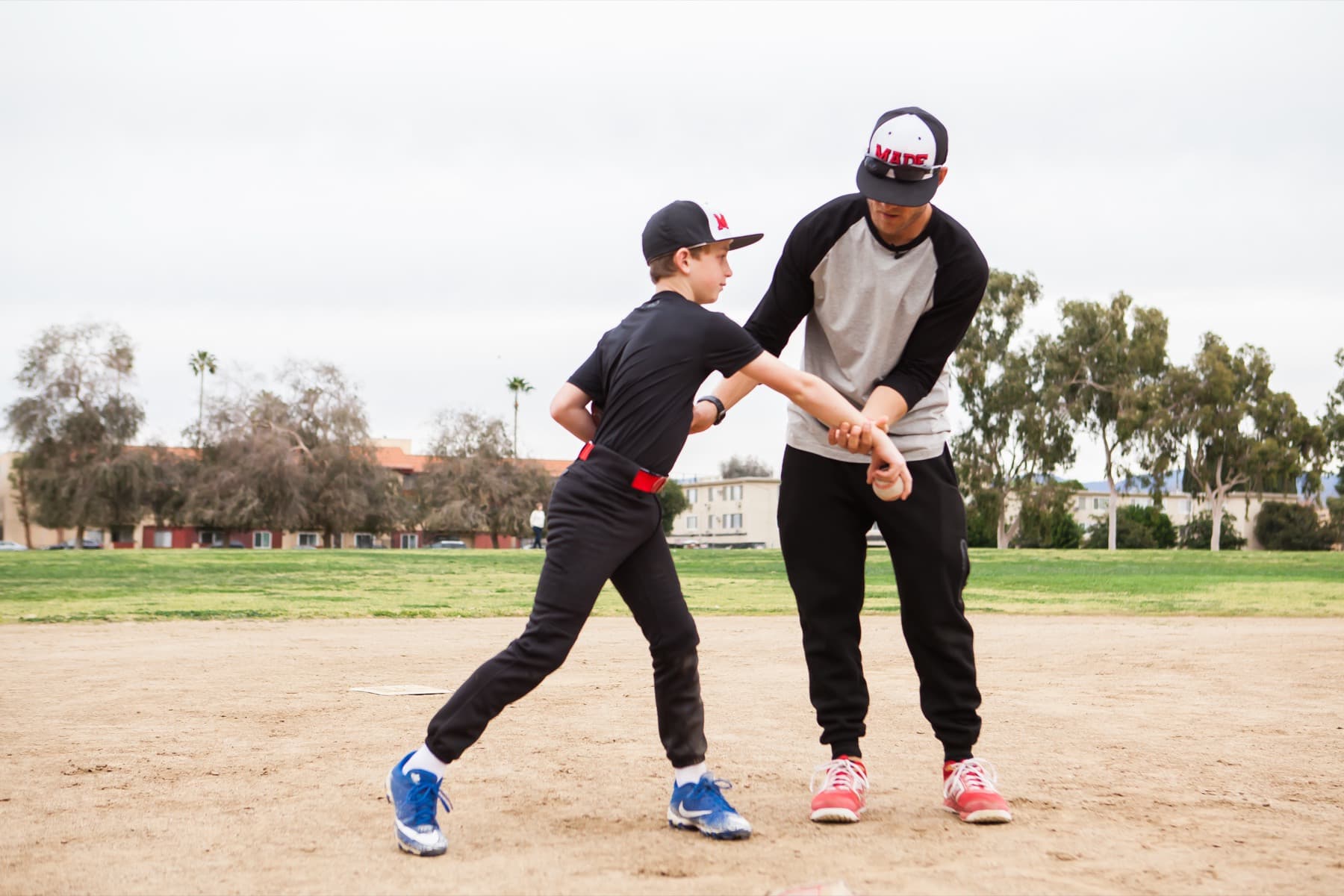 Coach Isaac Hess guiding a young pitcher's arm and hips through the throwing motion on a dirt infield