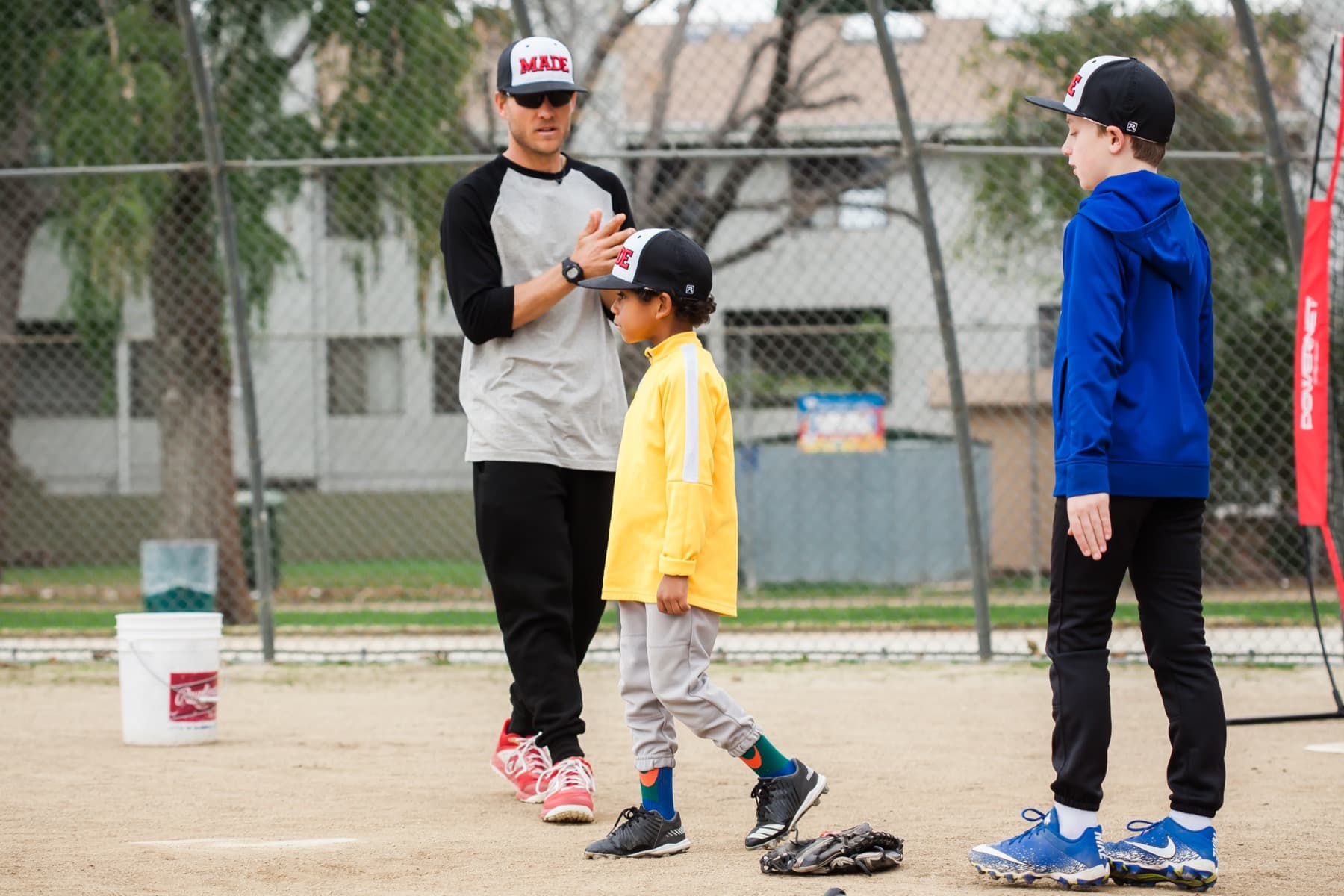Coach Isaac Hess talking with a young player in a yellow jacket between swings at the batting net
