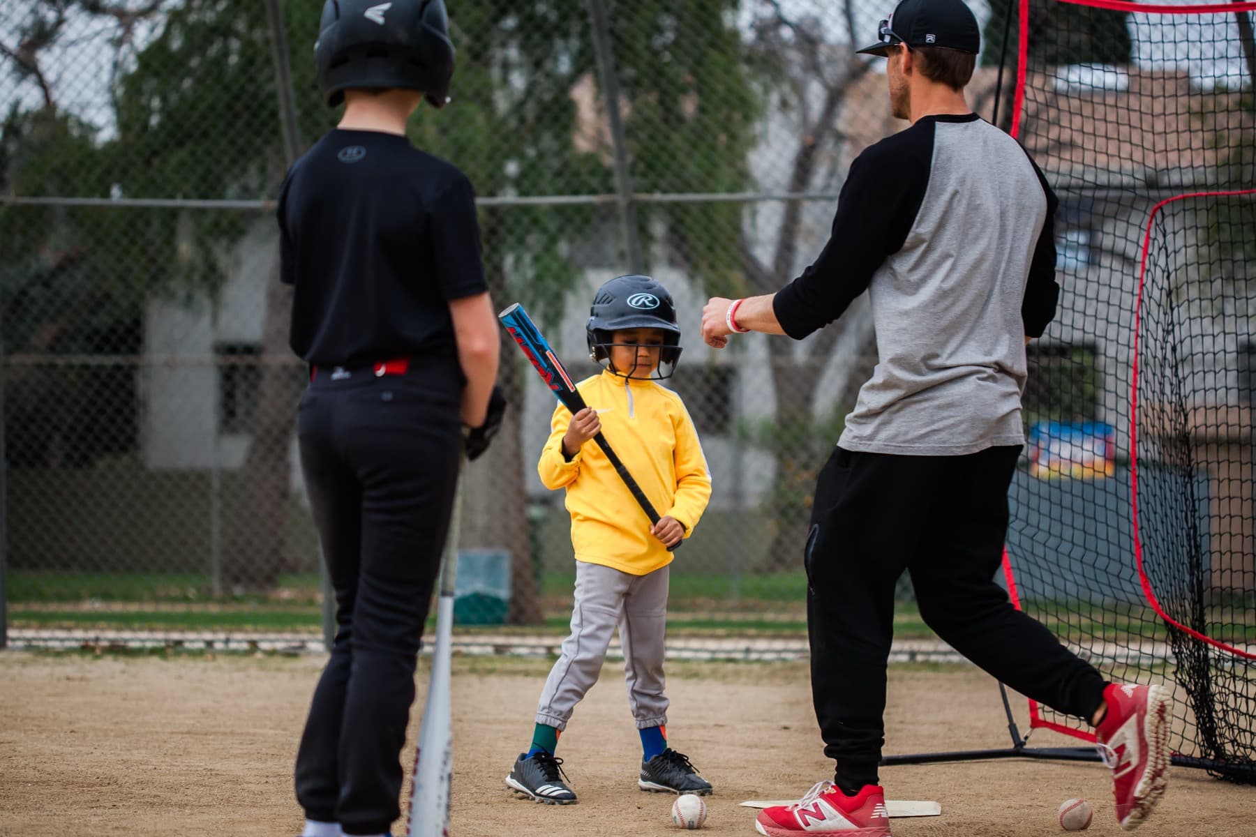 Coach Isaac Hess stepping in to work with a young batter at the plate while another player waits
