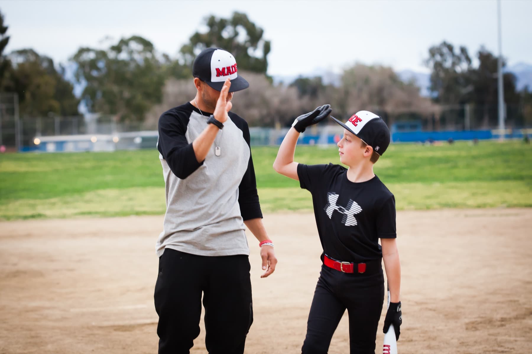 Coach Isaac Hess and a young player in a MADE cap sharing a high five