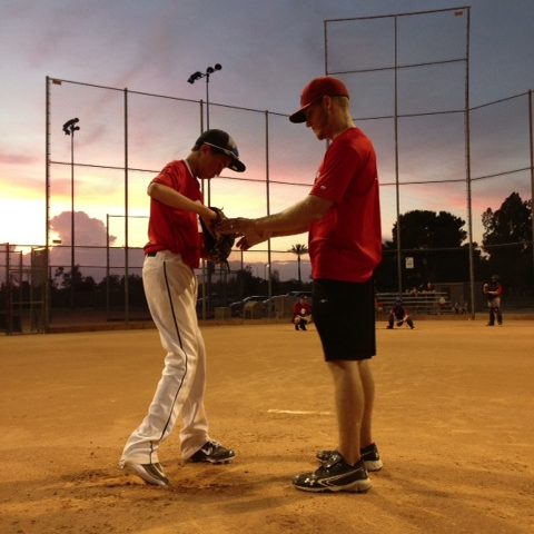A coach working with a young pitcher on the mound at dusk