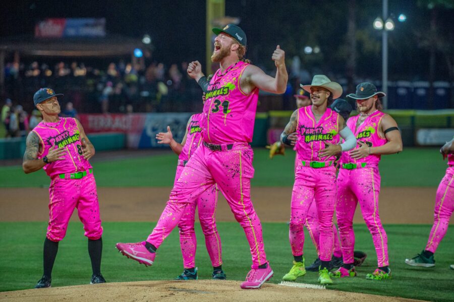 Party Animals baseball players celebrating on the mound in vibrant neon pink uniforms during a high-energy moment